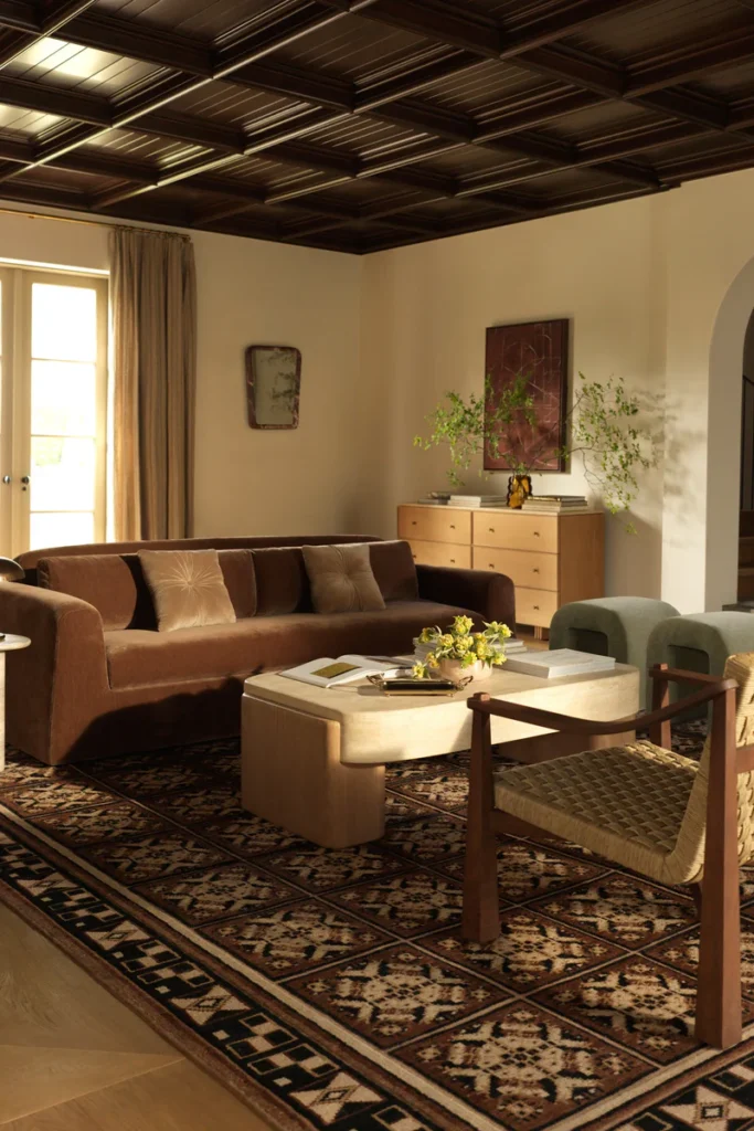 Lulu and Georgia Living Room – Polished Warmth design featuring a plush sofa, sculptural coffee table, accent chair, timeless rug, and warm lighting.